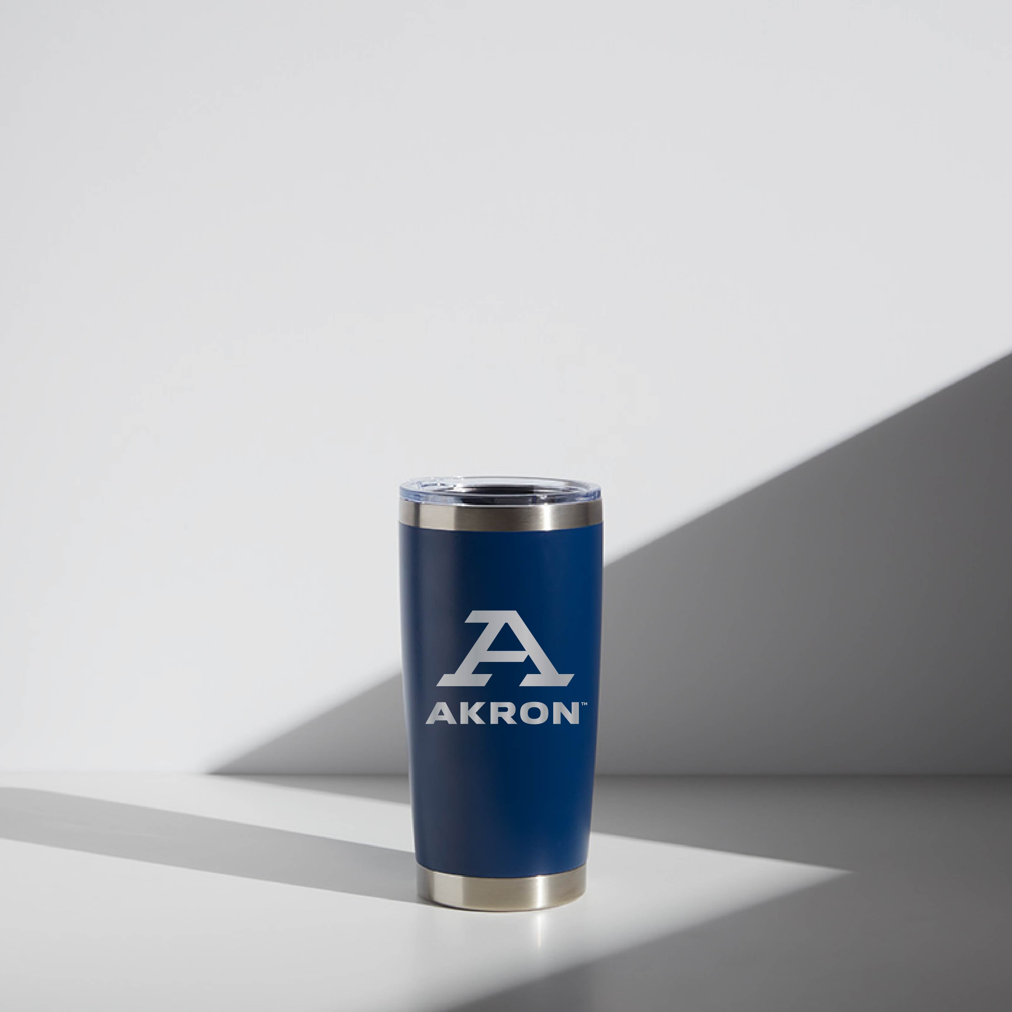 20 oz WATR tumbler branded with University of Akron logo and "Block A" design in white on a blue background, featuring a stainless steel rim and clear lid, positioned against a softly lit background.