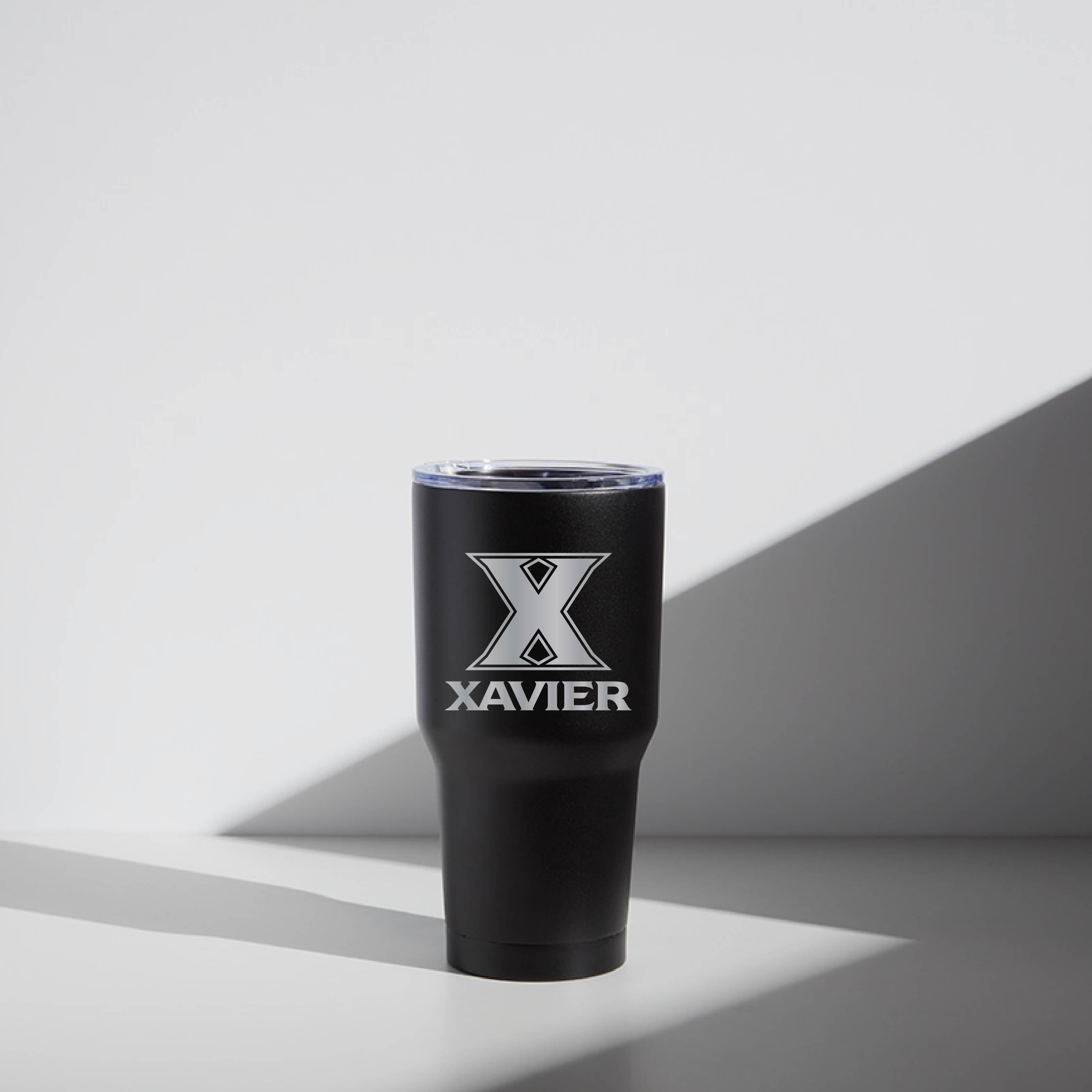 A black 30 oz stainless steel tumbler with the text 'XAVIER' printed on it, placed against a white background with a shadow cast beneath it.
