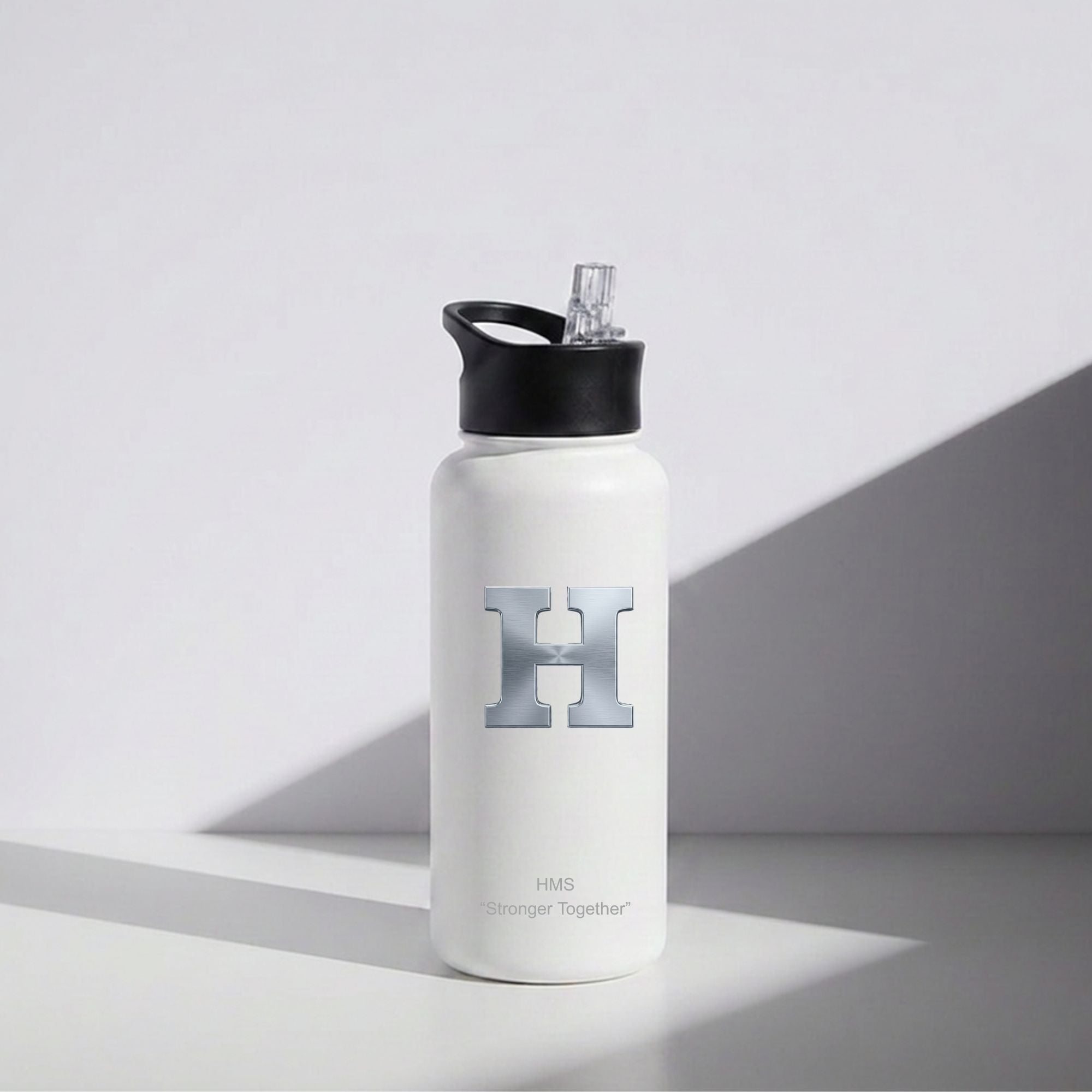 A white insulated water bottle with a black flip-top lid and a gray bee graphic on the front, standing on a white surface with a gray shadow cast by a diagonal light beam.