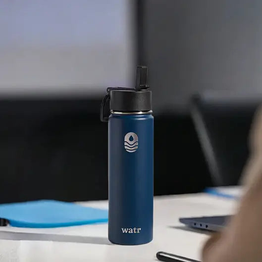 Custom navy blue Watr insulated water bottle with black sport lid, engraved with a water drop logo, on a conference table as a company picnic gift idea